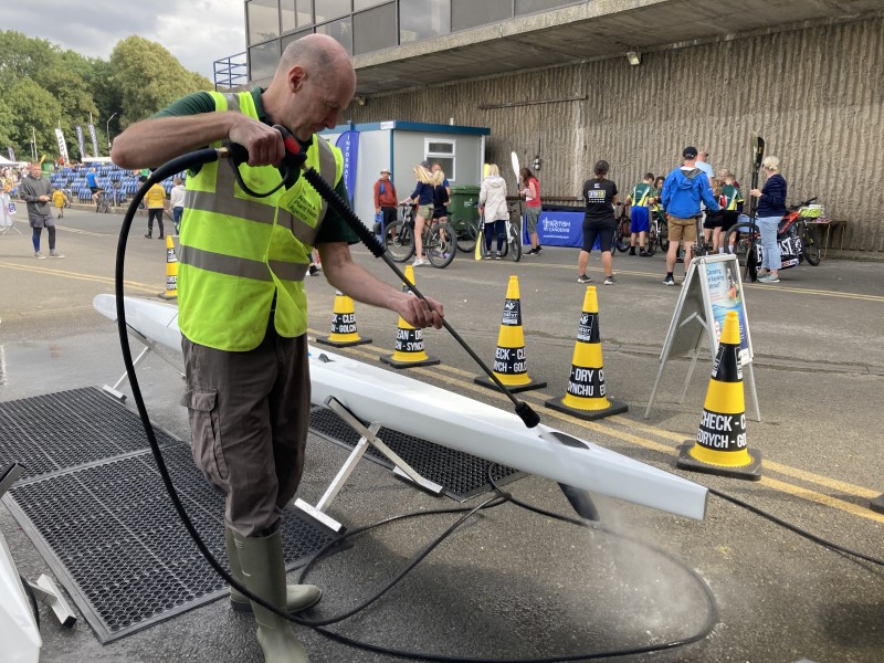 A man in a high-vis vest cleans a canoe with a pressure washer.