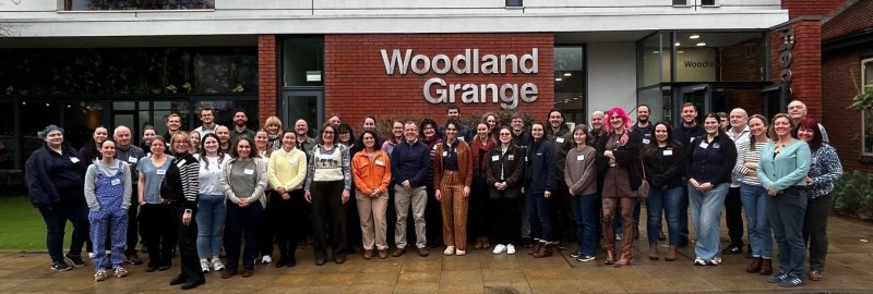 A large group of people standing in front of a brick building smiling at the camera